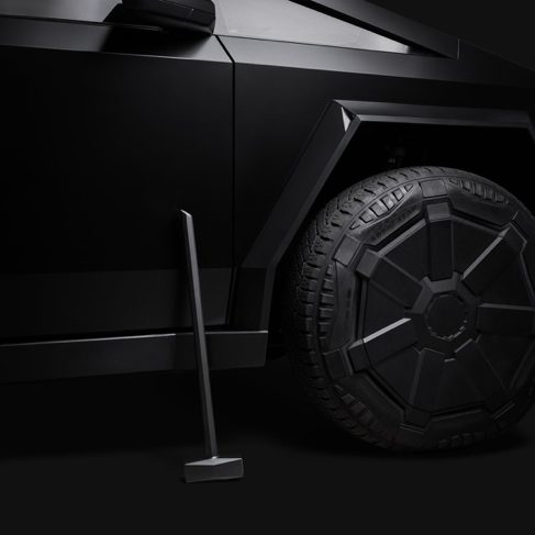 A CyberHammer leaning against a Cybertruck wheel, all matte black