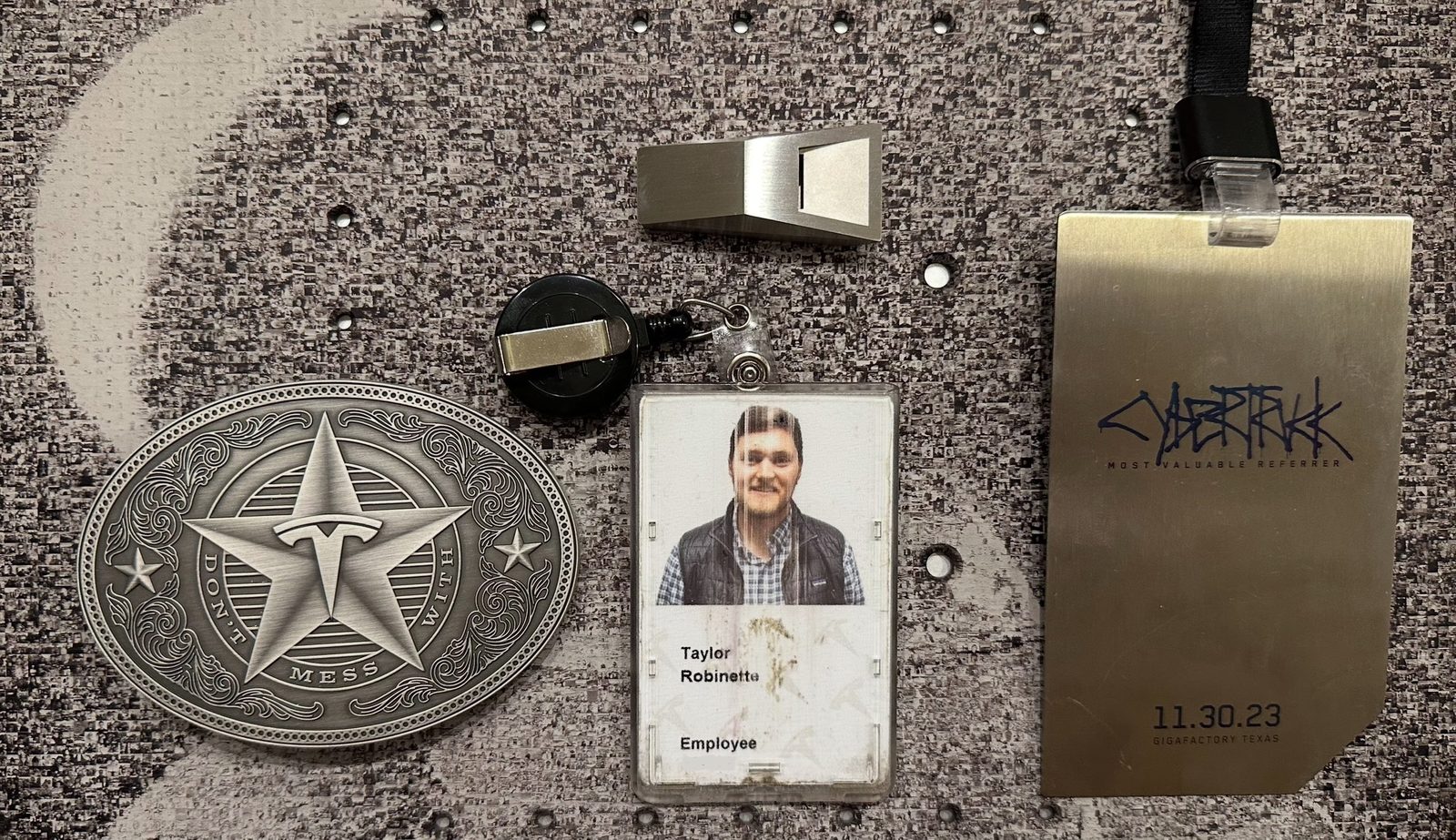 Tesla memorabilia on a photo mosaic background: a Don't Mess With Tesla belt buckle, employee badge, Cyberwhistle, and a Cybertruck Most Valuable Referrer pass dated November 30 2023