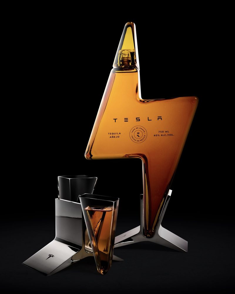 A lightning-bolt-shaped bottle of Tesla Tequila with two angular glasses on a black background