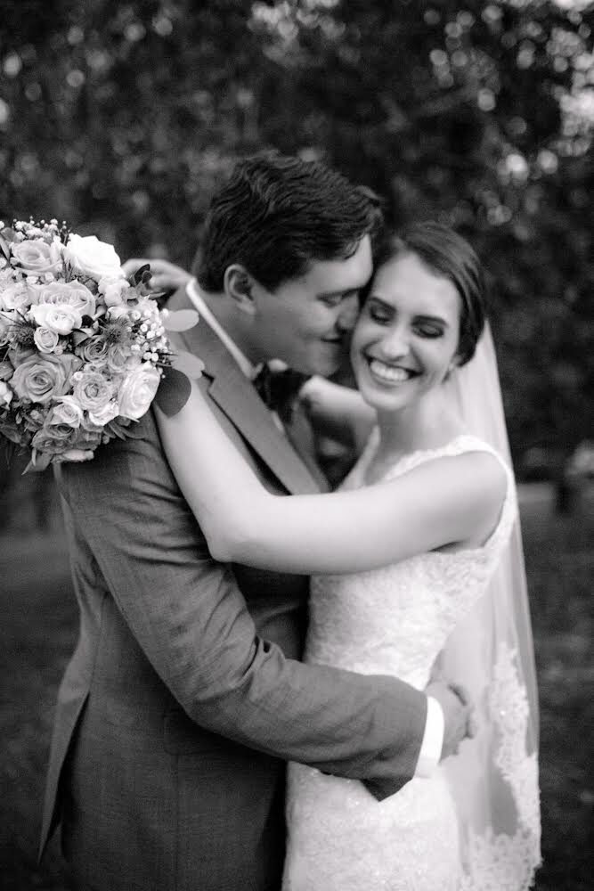Taylor and his wife on their wedding day, black and white, her bouquet over his shoulder